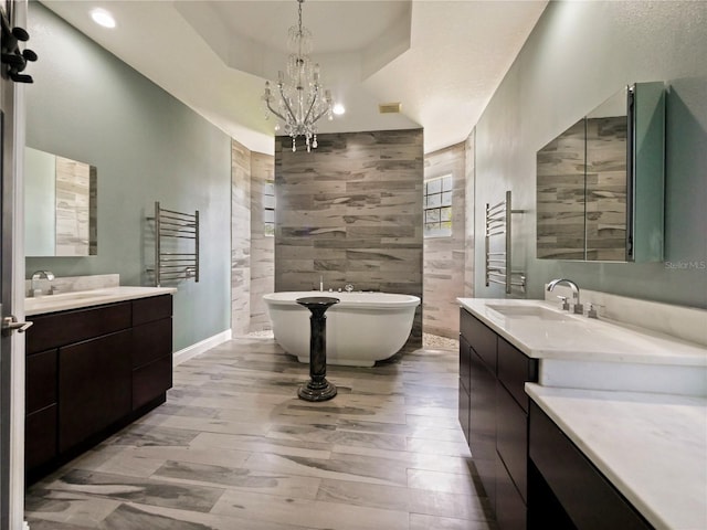 bathroom featuring a bathing tub, hardwood / wood-style flooring, vanity, a notable chandelier, and a tray ceiling