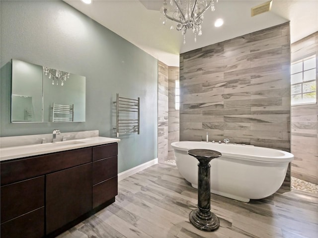 bathroom with tile walls, a tub to relax in, hardwood / wood-style flooring, vanity, and a notable chandelier