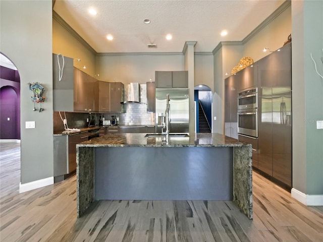 kitchen with tasteful backsplash, wall chimney range hood, light wood-type flooring, and appliances with stainless steel finishes