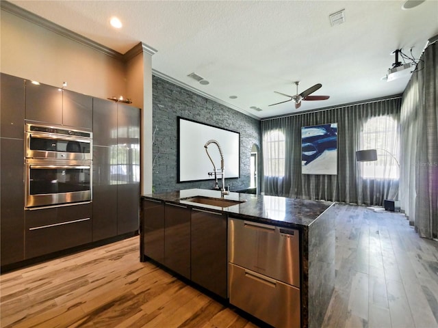 kitchen with ornamental molding, sink, double oven, and light wood-type flooring