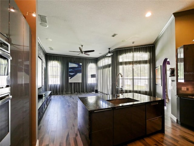 kitchen with sink, crown molding, dark hardwood / wood-style floors, dark brown cabinetry, and a center island with sink