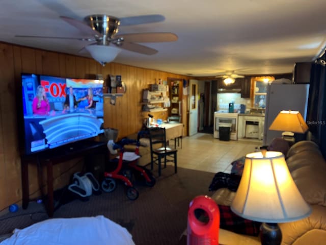 living room with ceiling fan, light tile patterned floors, and wooden walls