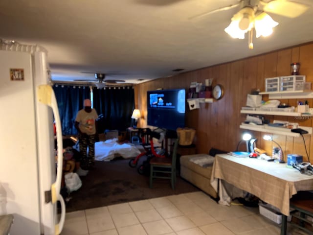 living room with ceiling fan, wood walls, and light tile patterned floors