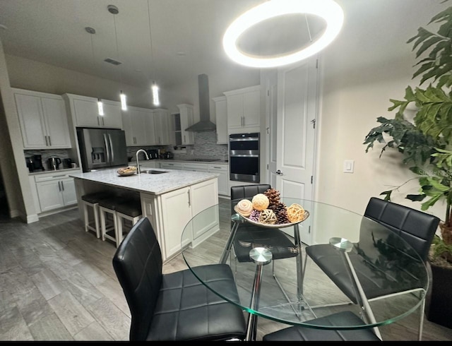 kitchen featuring sink, stainless steel appliances, wall chimney range hood, an island with sink, and decorative backsplash