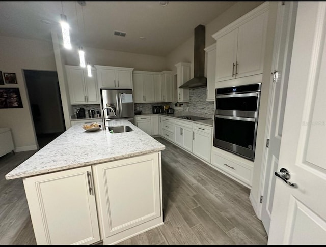 kitchen featuring pendant lighting, wall chimney range hood, sink, an island with sink, and appliances with stainless steel finishes