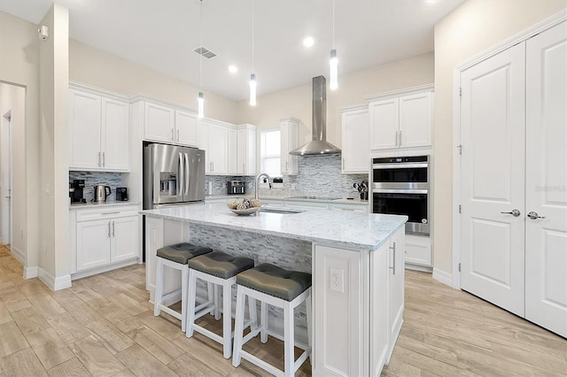 kitchen featuring visible vents, a sink, stainless steel appliances, white cabinets, and wall chimney exhaust hood