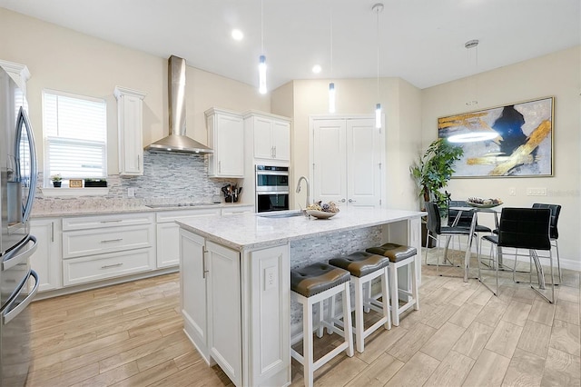 kitchen featuring wall chimney range hood, tasteful backsplash, white cabinetry, stainless steel appliances, and light wood finished floors