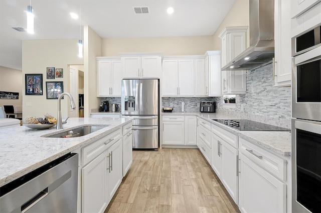 kitchen featuring visible vents, a sink, appliances with stainless steel finishes, white cabinetry, and wall chimney exhaust hood