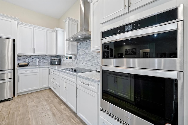 kitchen with decorative backsplash, white cabinets, stainless steel appliances, and wall chimney exhaust hood