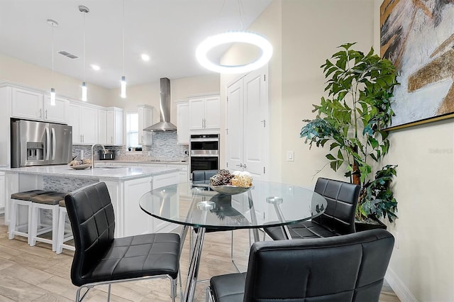 kitchen featuring visible vents, a sink, decorative backsplash, appliances with stainless steel finishes, and wall chimney range hood