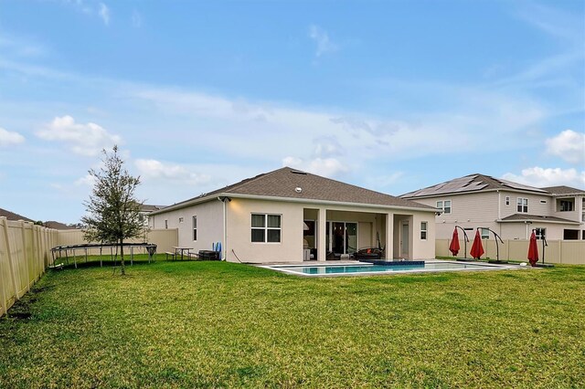 back of house with stucco siding, a trampoline, a fenced backyard, and a yard