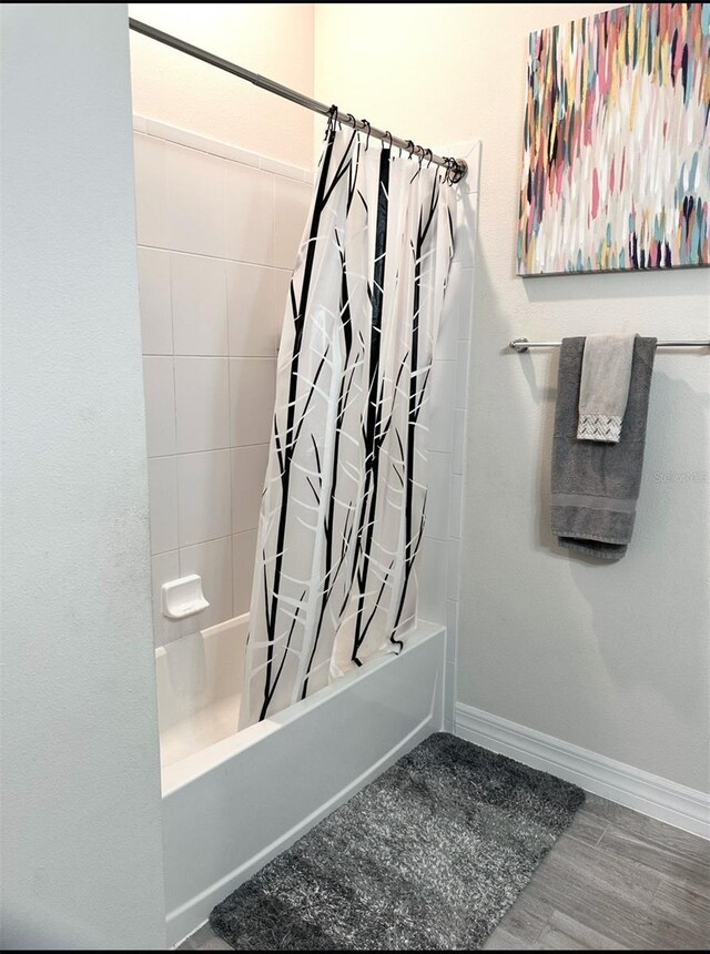 bathroom with wood finished floors, baseboards, and shower / bath combo with shower curtain