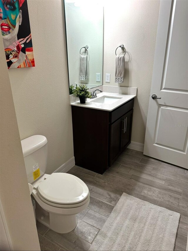 bathroom featuring baseboards, toilet, wood finished floors, and vanity