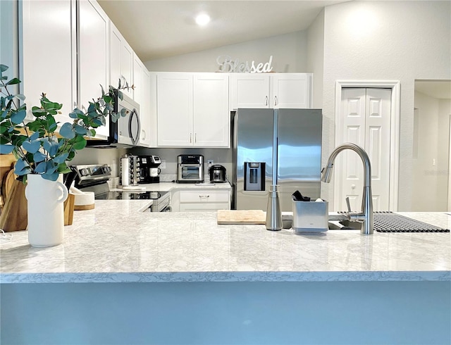 kitchen featuring white cabinets, appliances with stainless steel finishes, vaulted ceiling, and light stone countertops