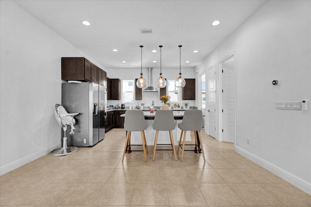 kitchen with dark brown cabinetry, a center island, stainless steel fridge, pendant lighting, and a kitchen bar