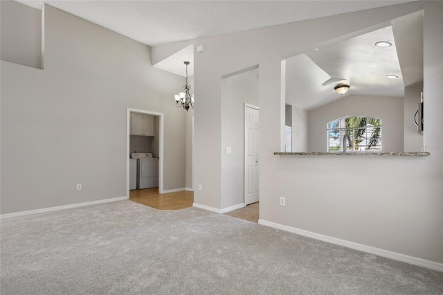 carpeted spare room with lofted ceiling, washing machine and clothes dryer, and an inviting chandelier