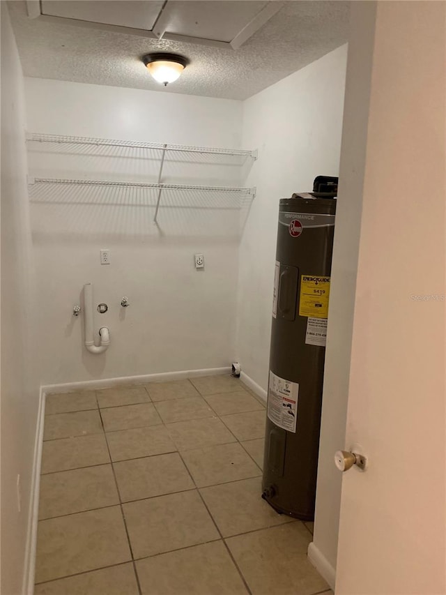 clothes washing area featuring a textured ceiling, electric water heater, tile patterned flooring, and hookup for a gas dryer