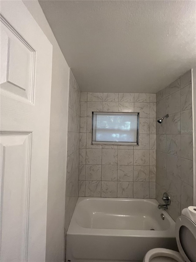 bathroom with tiled shower / bath, a textured ceiling, and toilet