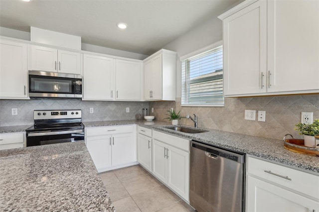 kitchen with light tile patterned floors, a sink, white cabinets, appliances with stainless steel finishes, and decorative backsplash