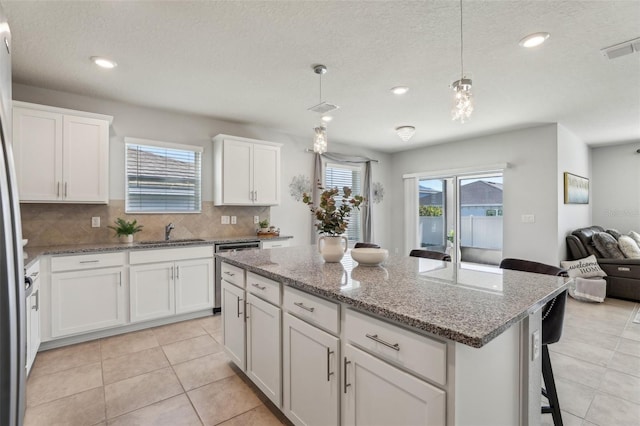 kitchen with a sink, visible vents, open floor plan, a center island, and tasteful backsplash