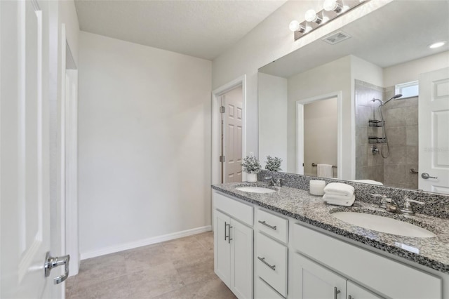 bathroom featuring visible vents, a sink, a tile shower, and baseboards