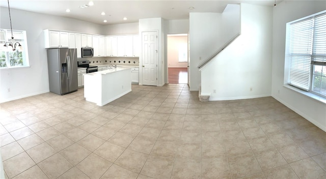 kitchen with appliances with stainless steel finishes, light tile patterned floors, white cabinets, pendant lighting, and a healthy amount of sunlight