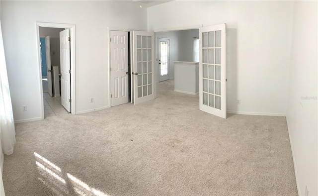 unfurnished bedroom featuring light colored carpet, ensuite bath, and french doors