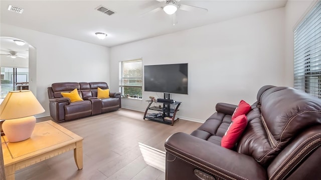 living room with visible vents, arched walkways, baseboards, ceiling fan, and light wood-style flooring