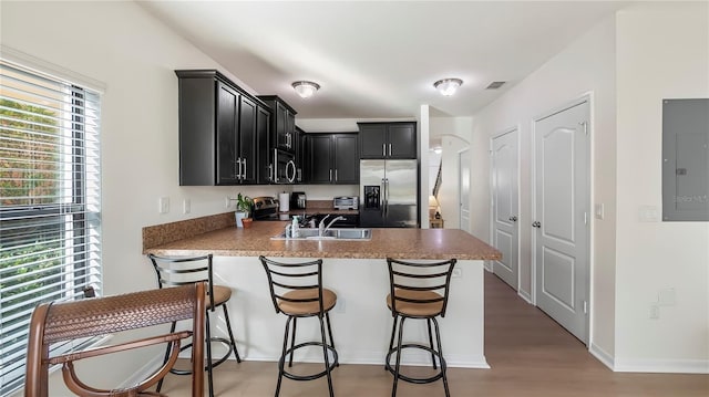 kitchen featuring electric panel, a kitchen breakfast bar, stainless steel appliances, dark cabinetry, and a sink