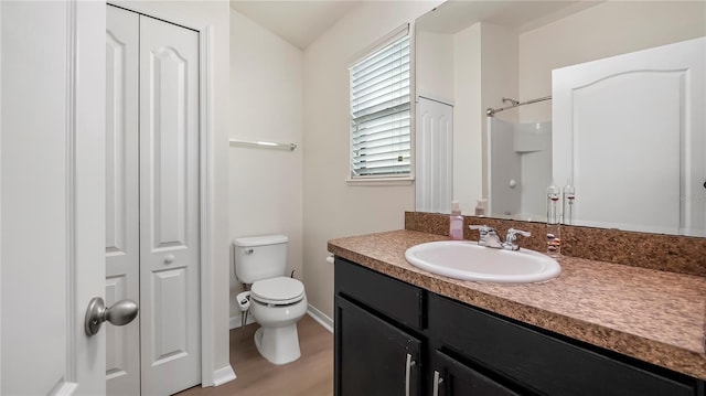 full bathroom with a closet, toilet, vanity, wood finished floors, and baseboards