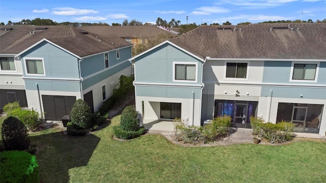 rear view of house with a shingled roof, a yard, a patio, and stucco siding