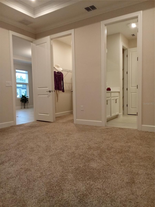 unfurnished bedroom with a closet, a spacious closet, crown molding, and light carpet