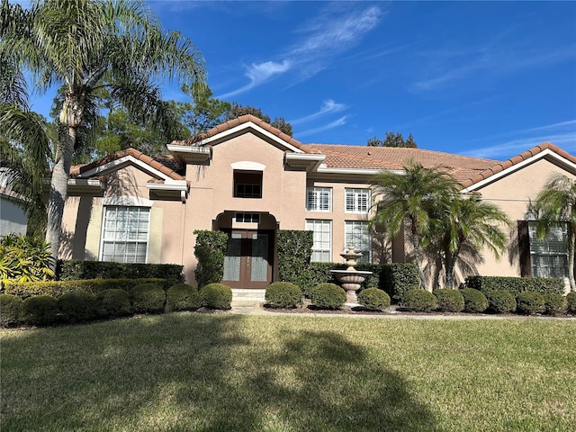 mediterranean / spanish home with a tiled roof, french doors, a front lawn, and stucco siding