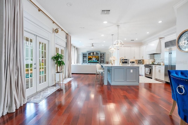 kitchen with white cabinetry, french doors, premium appliances, decorative light fixtures, and a kitchen island with sink