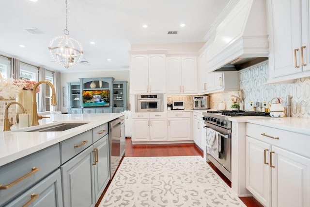 kitchen featuring gray cabinetry, white cabinetry, decorative light fixtures, custom exhaust hood, and appliances with stainless steel finishes