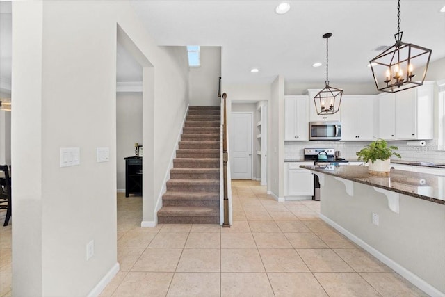 kitchen featuring white cabinets, appliances with stainless steel finishes, decorative light fixtures, and dark stone countertops