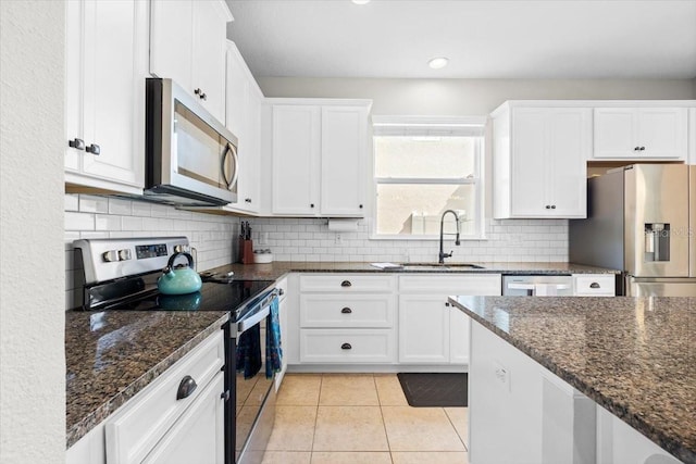 kitchen featuring white cabinetry, sink, dark stone counters, light tile patterned flooring, and appliances with stainless steel finishes