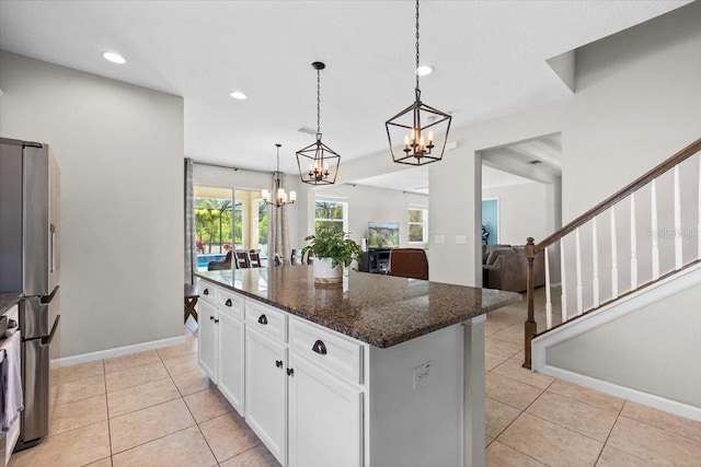 kitchen with a center island, dark stone counters, hanging light fixtures, stainless steel fridge, and white cabinetry