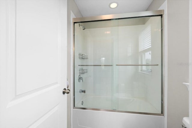 bathroom with toilet and shower / bath combination with glass door