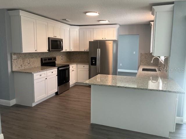 kitchen featuring kitchen peninsula, light stone countertops, stainless steel appliances, sink, and white cabinets