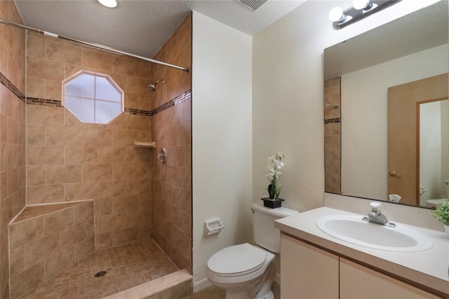 bathroom featuring vanity, toilet, a textured ceiling, and a tile shower