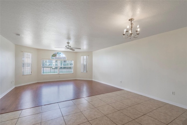 tiled spare room with ceiling fan with notable chandelier and a textured ceiling