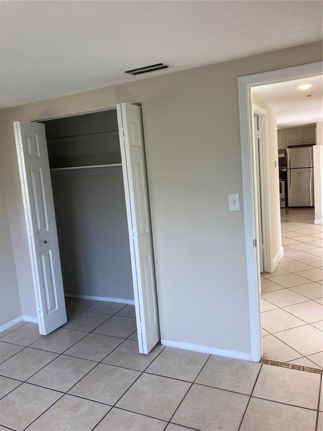 unfurnished bedroom featuring stainless steel fridge, light tile patterned floors, and a closet