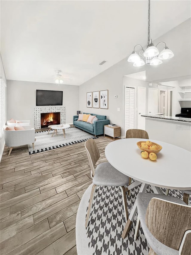 dining space with vaulted ceiling, a notable chandelier, and a tiled fireplace