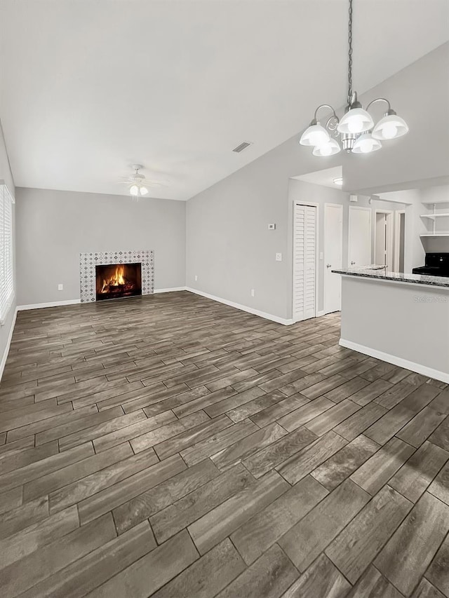 unfurnished living room with ceiling fan with notable chandelier and a fireplace