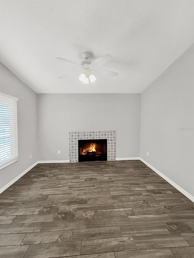 unfurnished living room with ceiling fan, a fireplace, and dark wood-type flooring