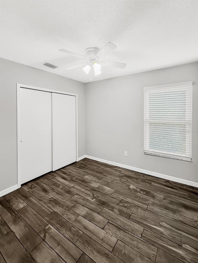 unfurnished bedroom with a textured ceiling, a closet, dark wood-type flooring, and ceiling fan