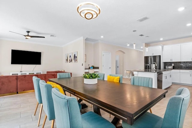 tiled dining area with sink, ceiling fan, and crown molding