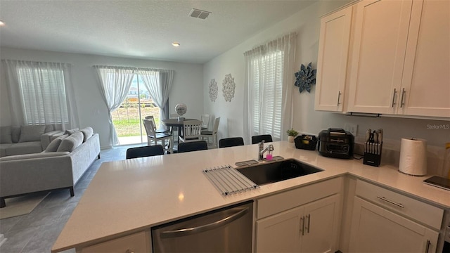 kitchen with white cabinets, sink, stainless steel dishwasher, tile patterned flooring, and kitchen peninsula