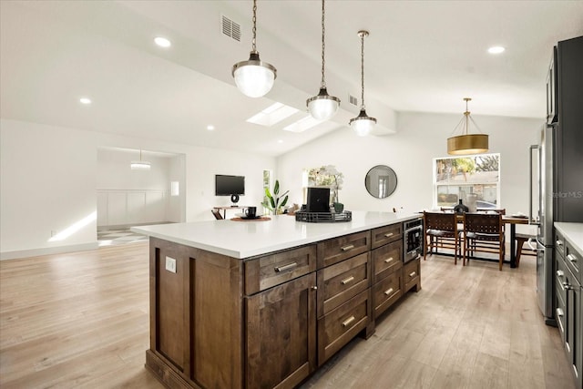 kitchen featuring vaulted ceiling with skylight, light wood-style flooring, a center island, decorative light fixtures, and light countertops